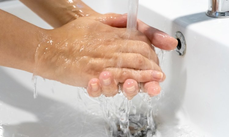 Nahaufnahme sich im Waschbecken waschender Hände unter klarem, laufendem Wasser 